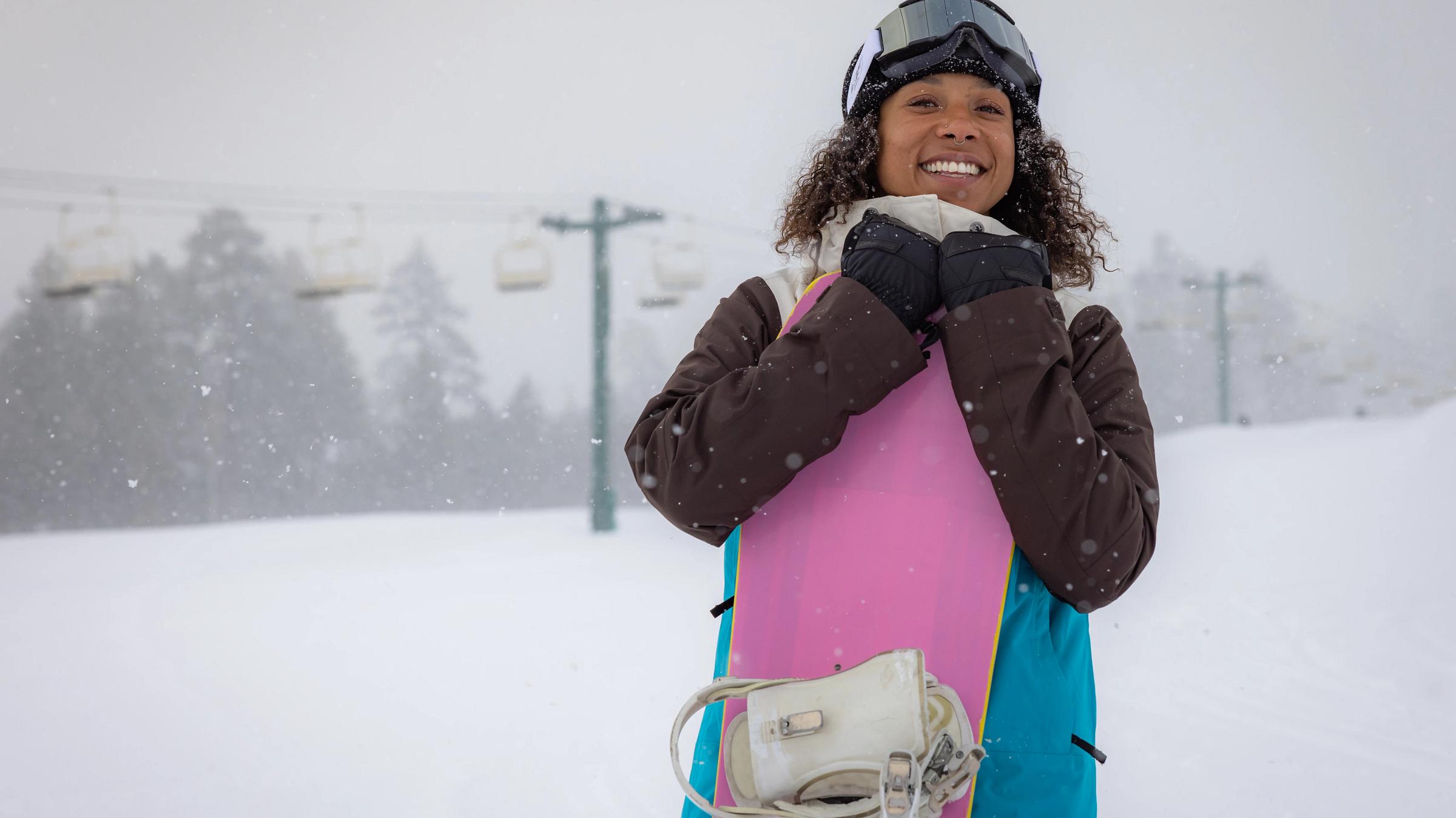 girl in snowboard gear, smiling and staring at the camera on the snow at big bear